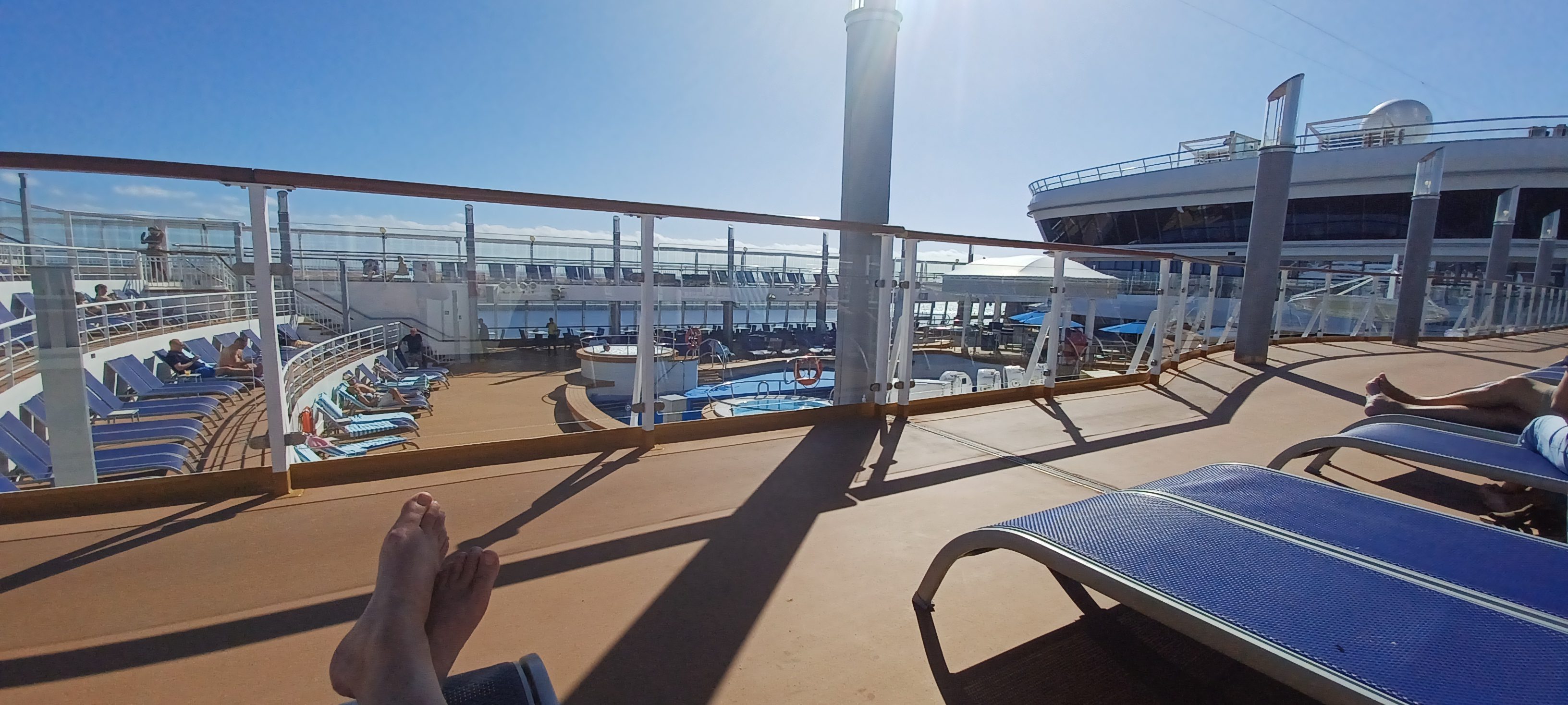 a person sitting on a deck with a pool and a ship in the background