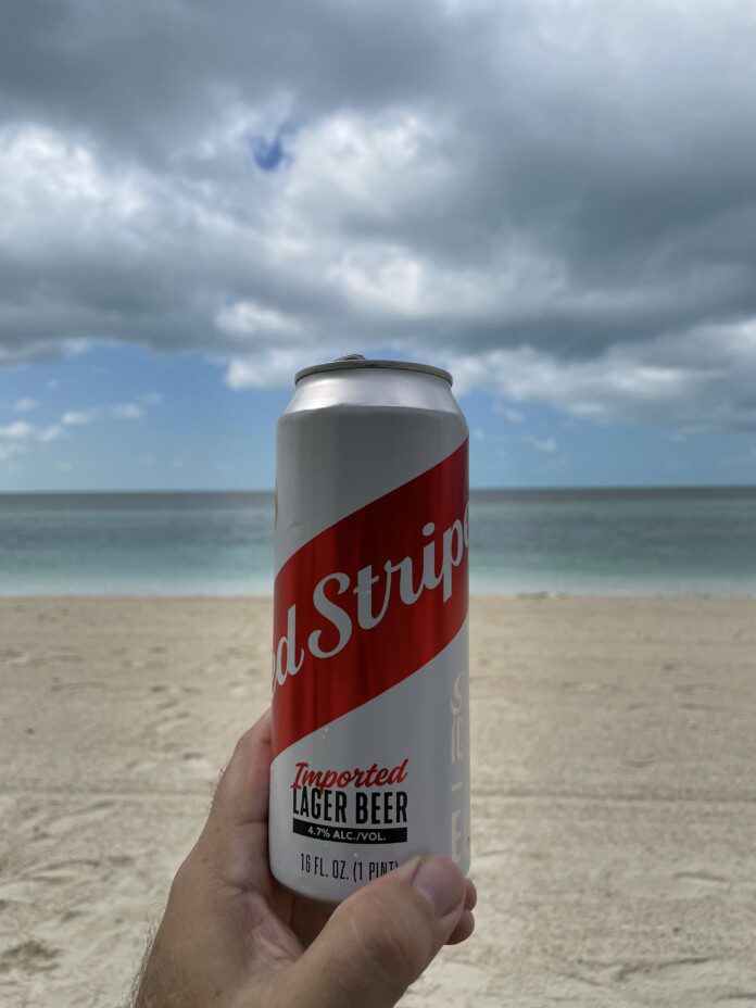 a hand holding a can of beer on a beach