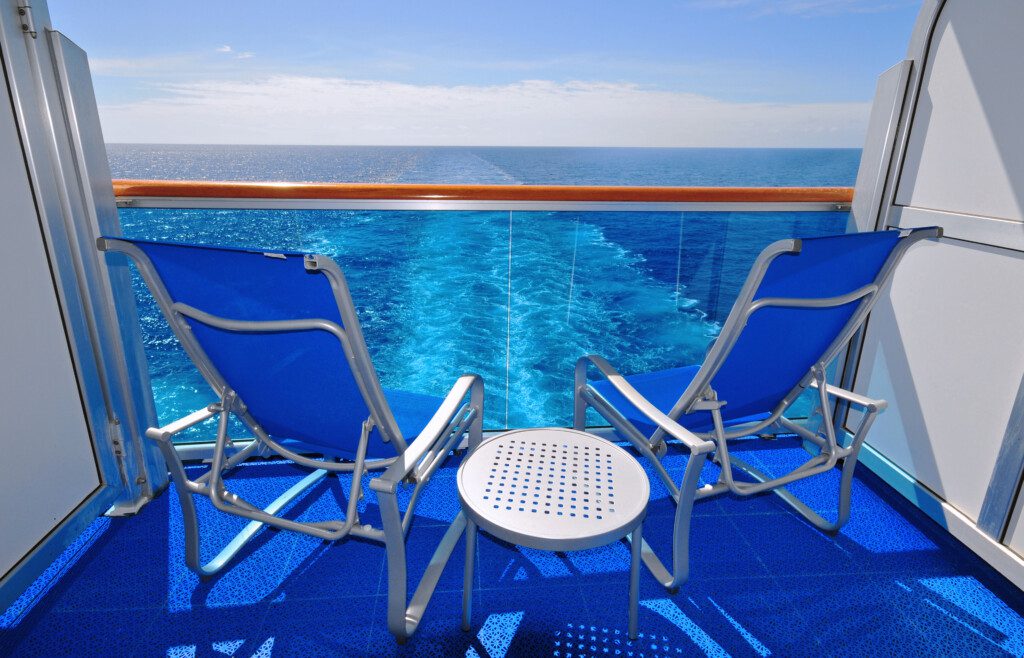 Two empty chairs on a cruise ship balcony overlook the wake of the ship