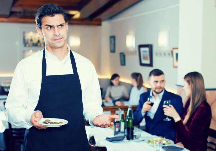 Portrait of waiter dissatisfied with small tip from cafe visitors (©iStock.com/JackF)