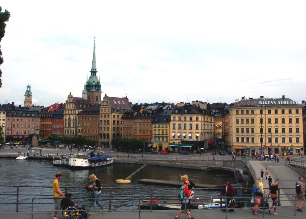 a group of people walking on Gamla stan over a river