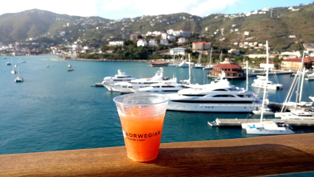 a cup of orange liquid on a railing with boats in the background