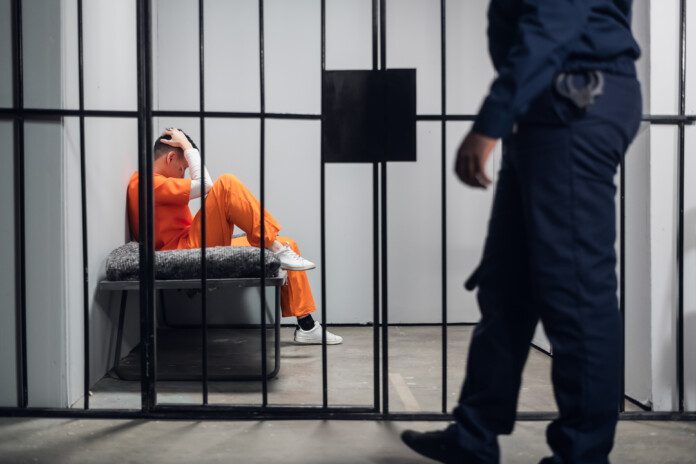 a man in orange jumpsuit sitting in a prison cell