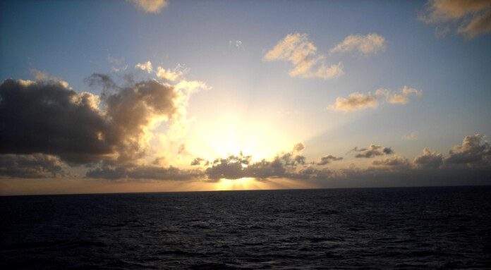 a sun shining through clouds over the ocean