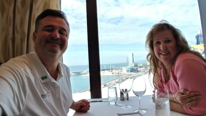 a man and woman sitting at a table with wine glasses and a view of the ocean