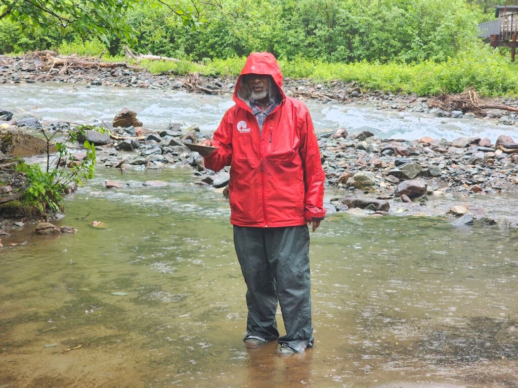 a man standing in a stream wearing a red jacket and standing in water