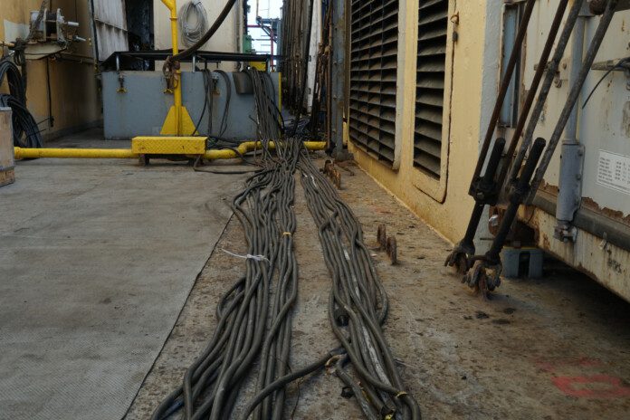 Spaghetti of black cables extended on the main deck from white reefer containers to the engine room through skylight on the container vessel.