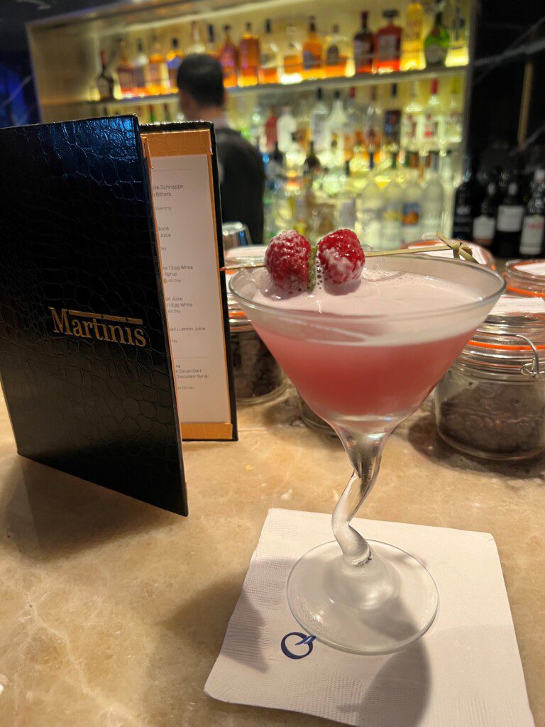 a pink drink with raspberries in a martini glass