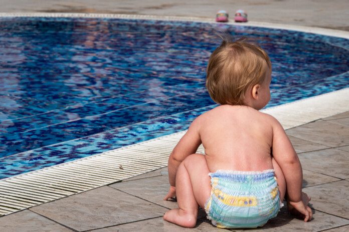 A closeup shot of a cute baby boy playing next to the swimming pool