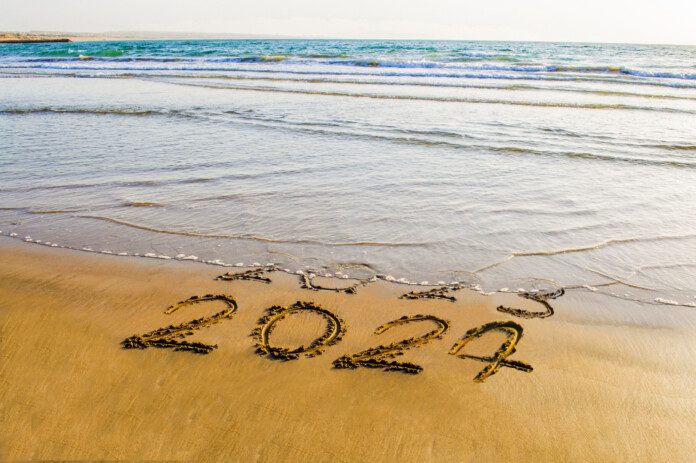 happy new year 2024 text on the sea beach. Abstract conceptual photo of coming New Year 2024 and leaving year of 2023, a clean handwritten new year greetings on a shoreline (©iStock.com/prospective56)