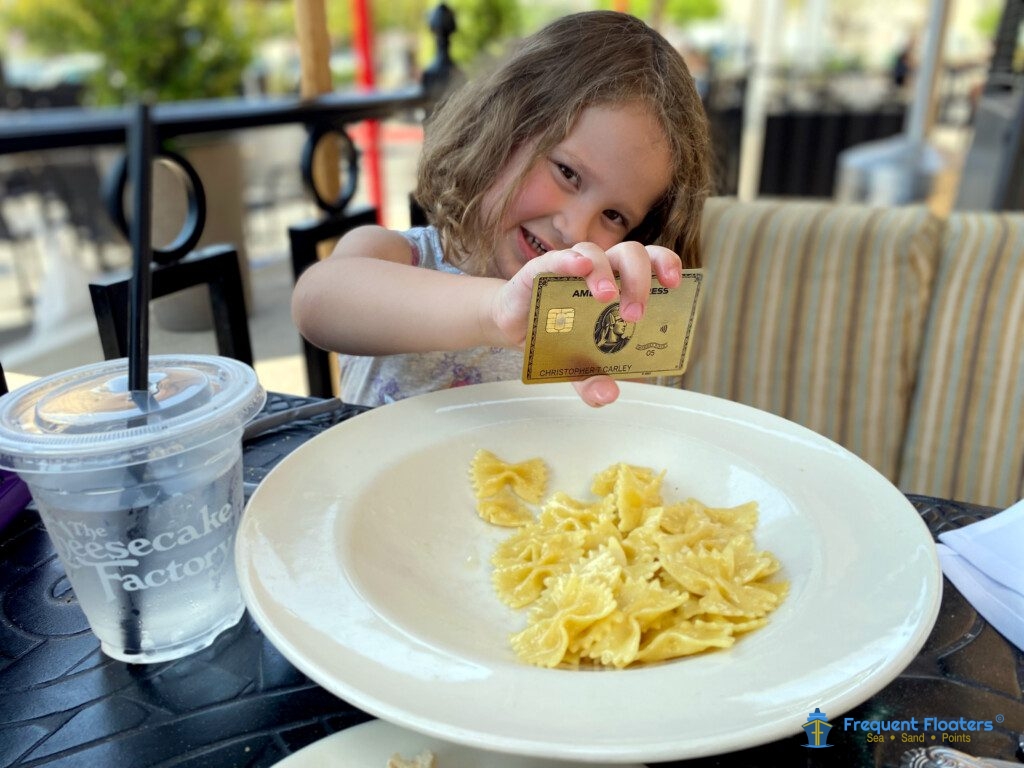 A little girl holding an Amex Gold Card during lunch at a Cheesecake Factory