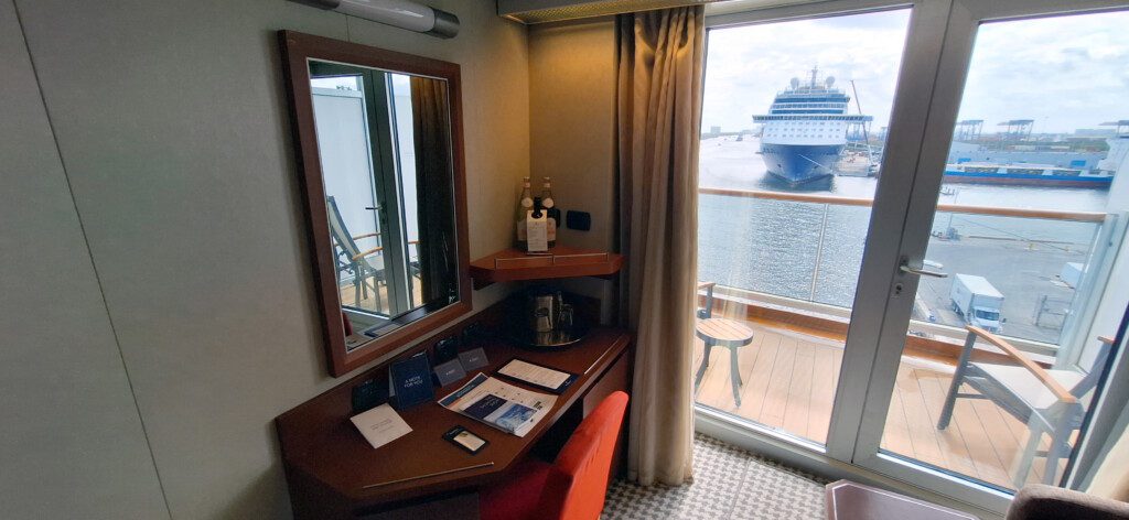 a desk with a mirror and a chair in a room with a cruise ship in the background