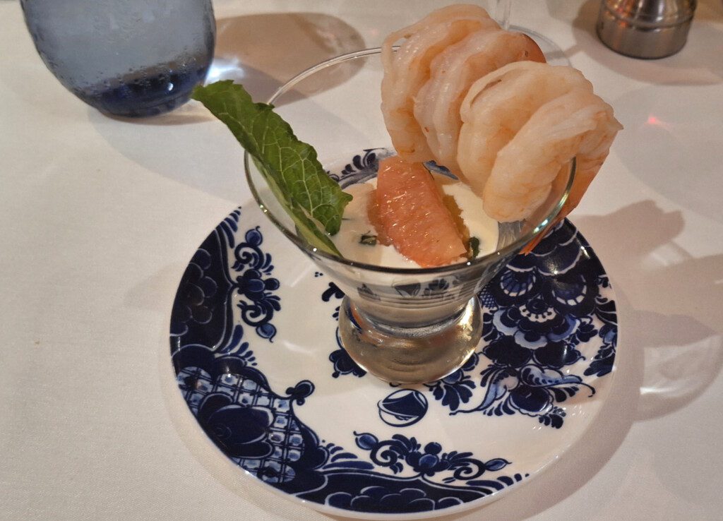 a plate with a glass of shrimp and a leaf on it