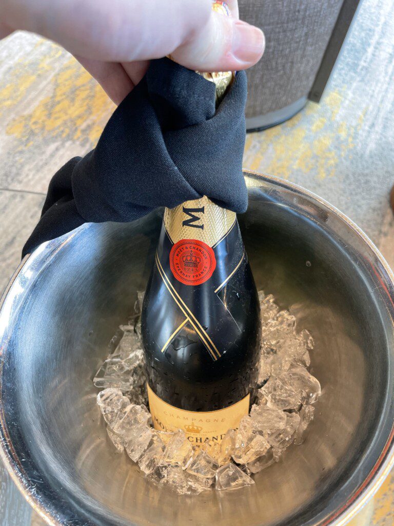 a hand holding a black cloth wrapped around a bottle of champagne in a silver bowl
