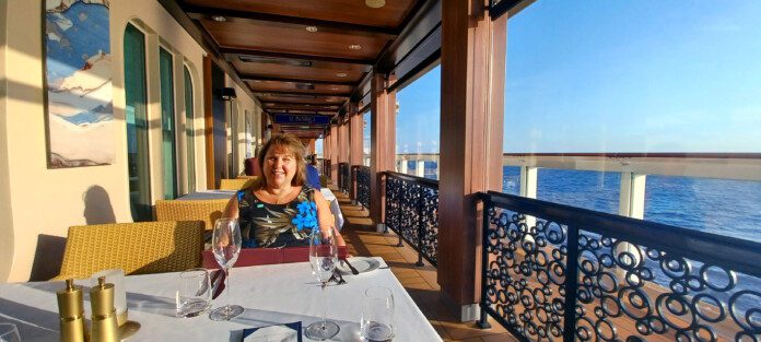 a woman sitting at a table with wine glasses on a deck