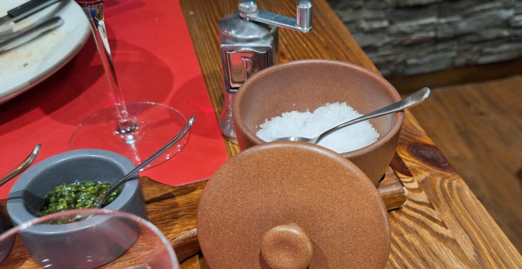 salt in a bowl with a spoon and a grinder on a table