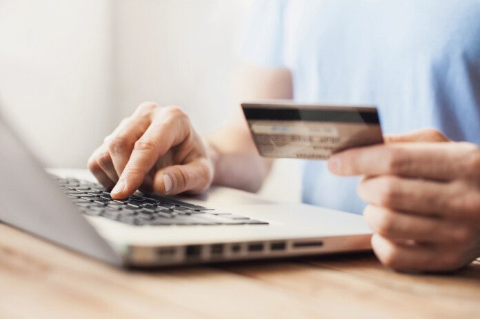 a person holding a credit card and typing on a laptop