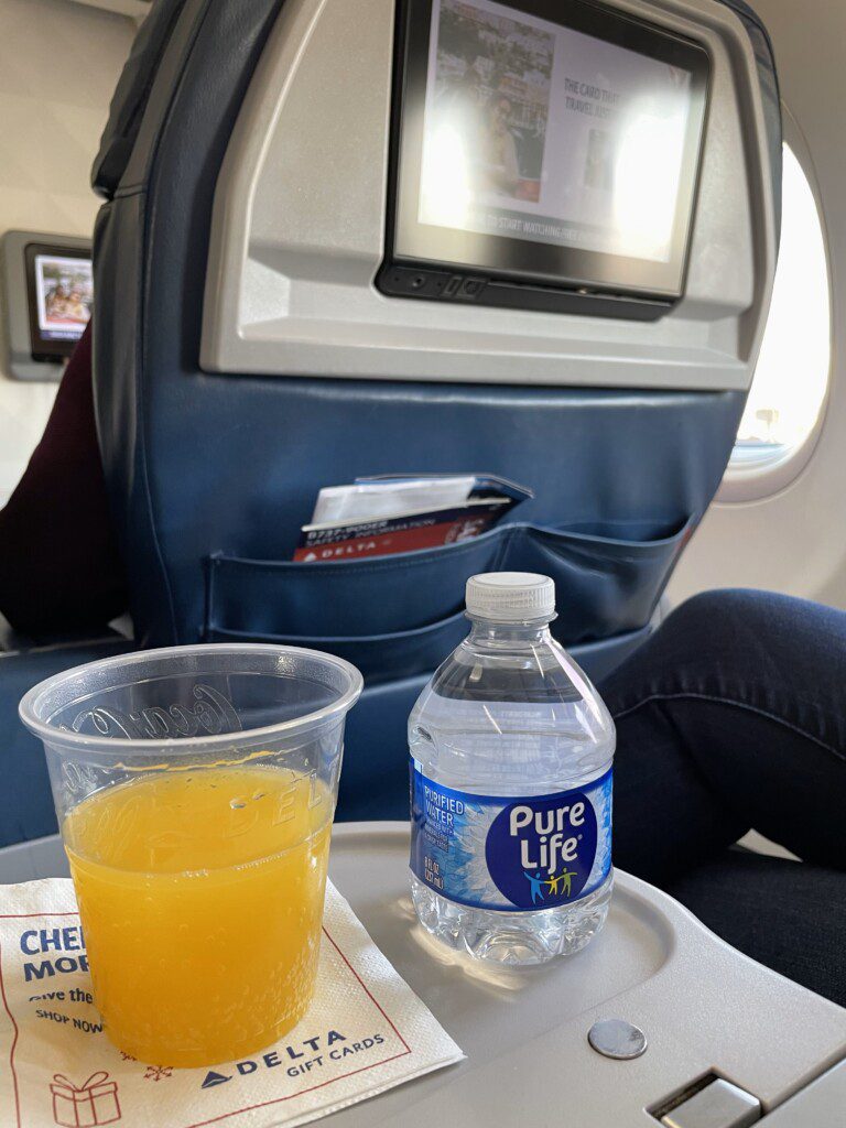 a drink and a plastic cup on a tray in a plane
